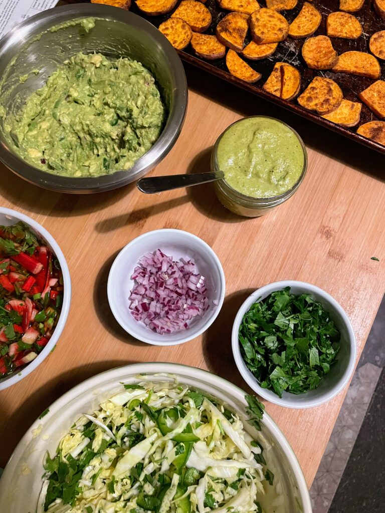 Image of roasted sweet potatoes, guacamole, salsa, slaw, and other taco toppings.
